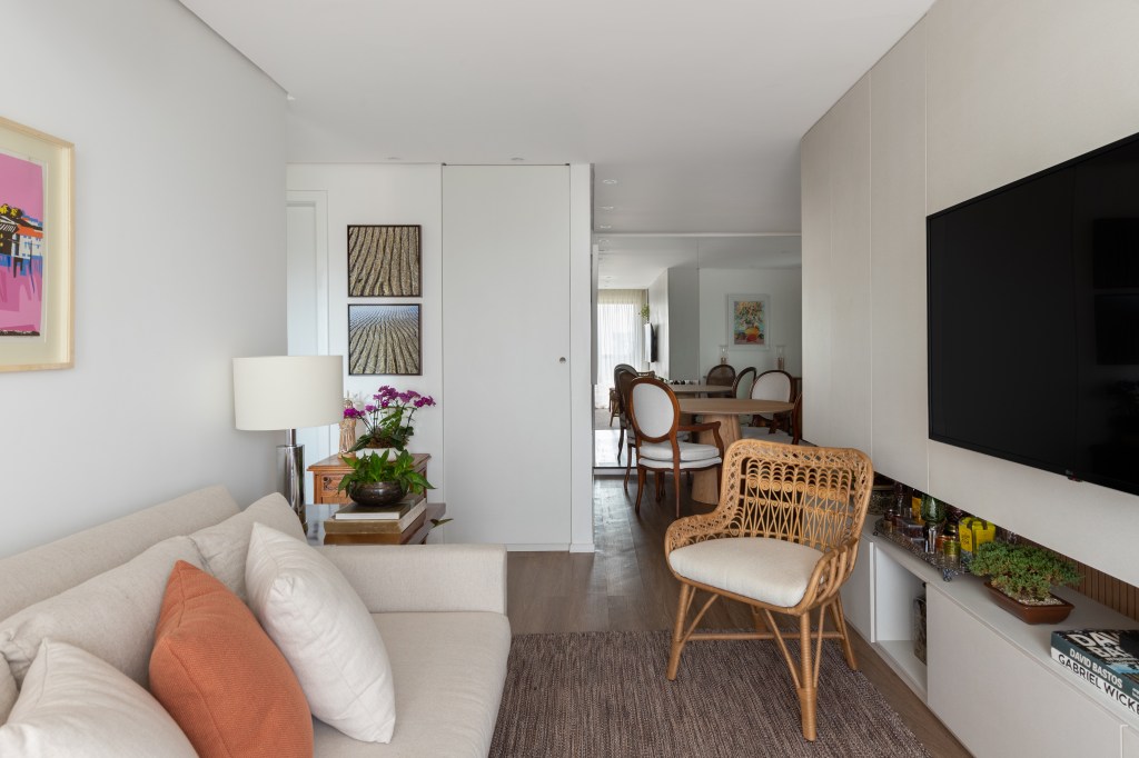Sala de estar pequena clara com paredes branca e sofá branco, cadeira de palhinha;