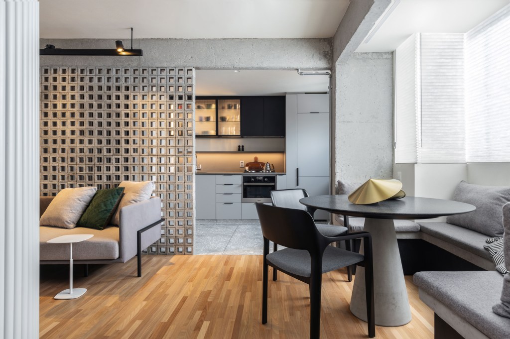 Sala de estar integrada com jantar com piso de madeira e mesa pequena redonda. Cozinha integrada com marcenaria branca e preta.