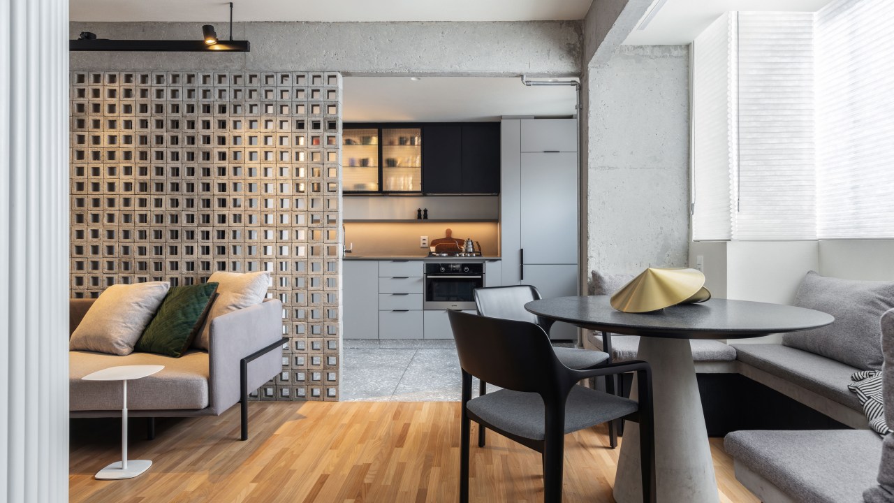 Sala de estar integrada com jantar com piso de madeira e mesa pequena redonda. Cozinha integrada com marcenaria branca e preta.