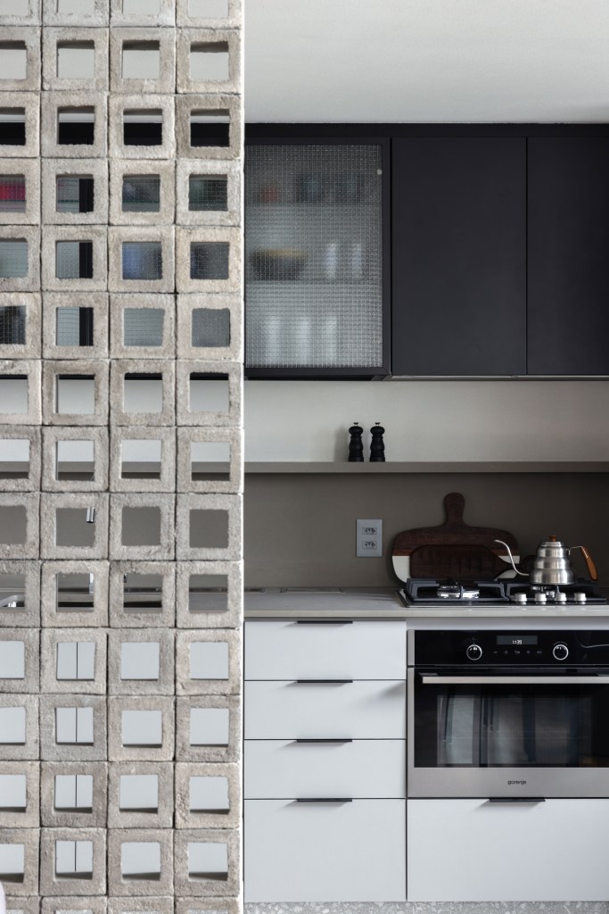 Cozinha integrada com marcenaria branca e armários superiores pretos com portas de vidro.