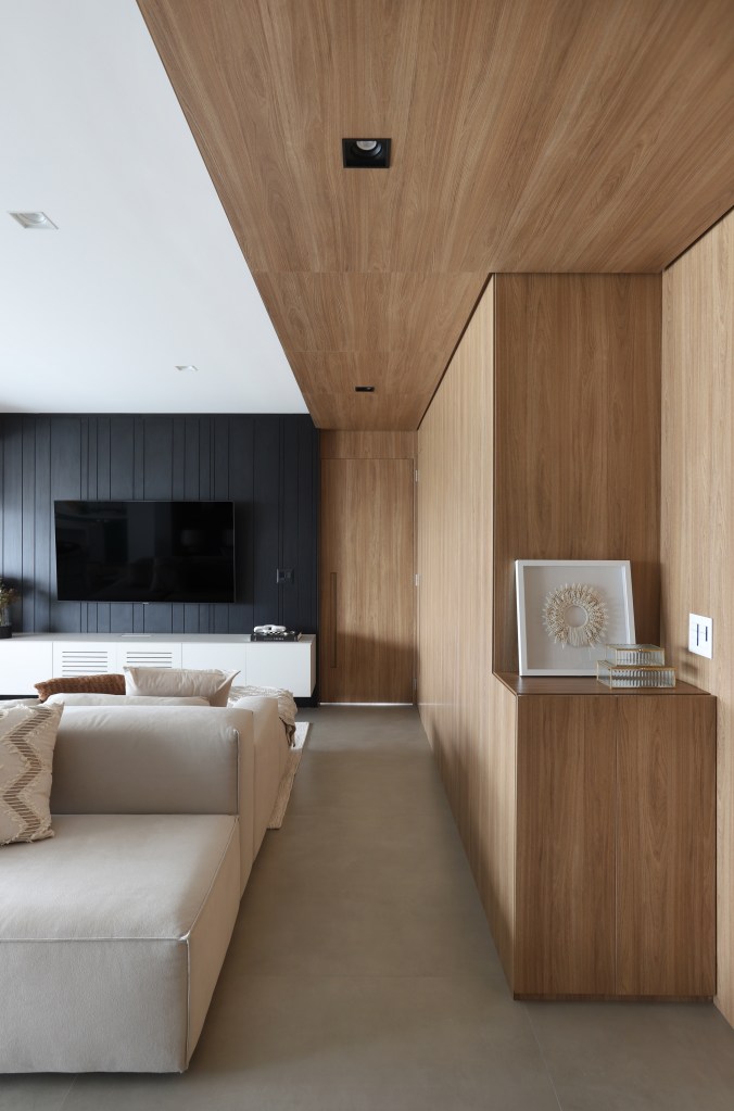 Painel de madeira percorre parede e teto da área social do apê de 120 m². Projeto Fantato Nitoli Arquitetura. Na foto, sala de estar com sapateira, painel de madeira e parede ripada.