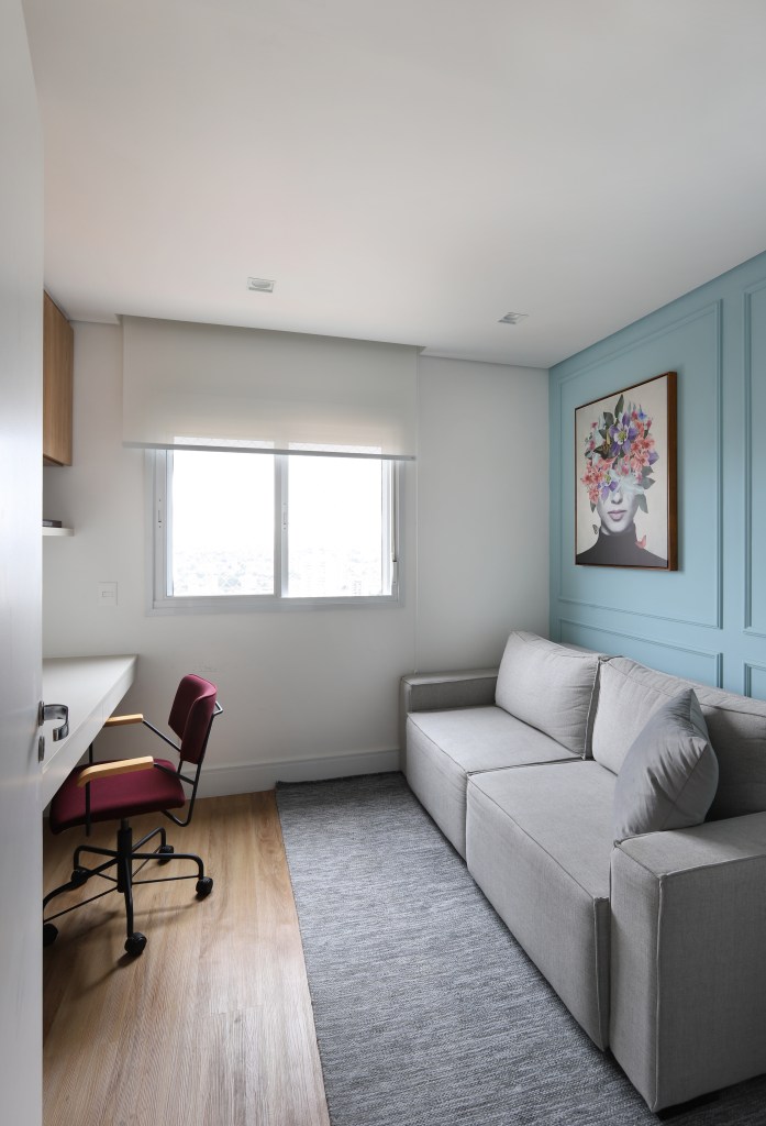 Painel de madeira percorre parede e teto da área social do apê de 120 m². Projeto Fantato Nitoli Arquitetura. Na foto, home office com parede azul e sofá cinza.