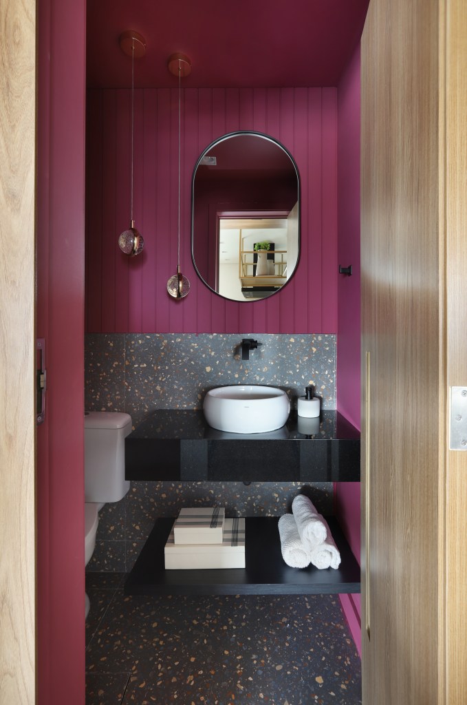 Painel de madeira percorre parede e teto da área social do apê de 120 m². Projeto Fantato Nitoli Arquitetura. Na foto, lavabo com parede marsala e porcelanato que imita granilite. Espelho oval.