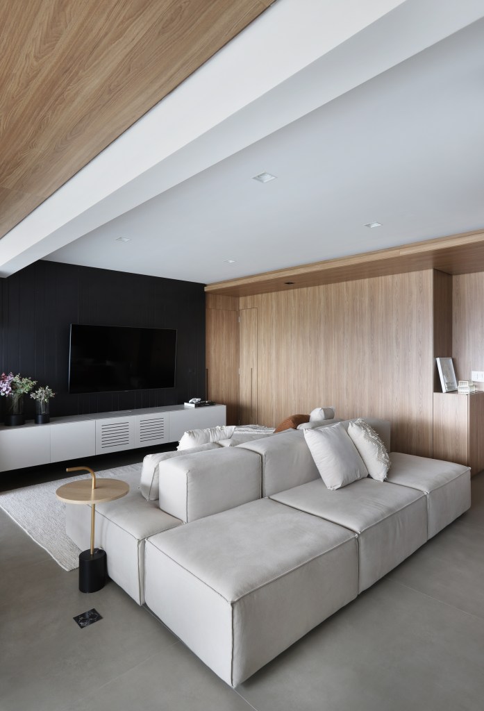 Painel de madeira percorre parede e teto da área social do apê de 120 m². Projeto Fantato Nitoli Arquitetura. Na foto, sala de estar com sofa ilha, parede de madeira e tv.