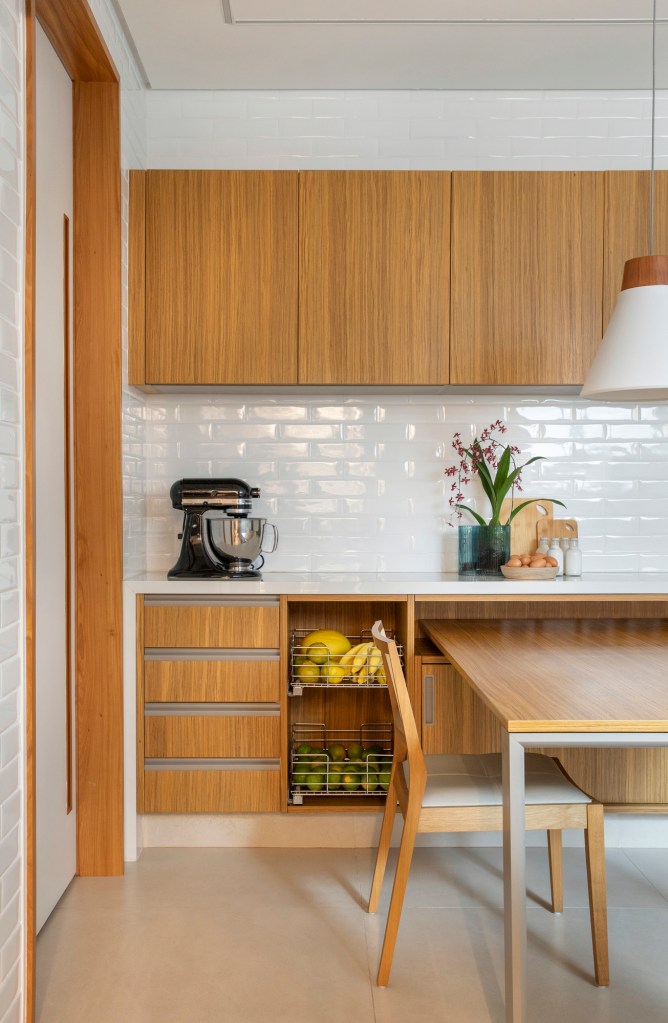 Cozinha com marcenaria na cor madeira, copa e backsplash de tijolinhos brancos tipo subway tiles.