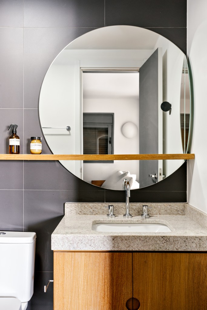 Banheiro com espelho em formato orgânico e prateleira de madeira.