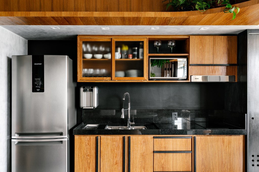 Cozinha com armários de madeira e portas de vidro, parede preta.