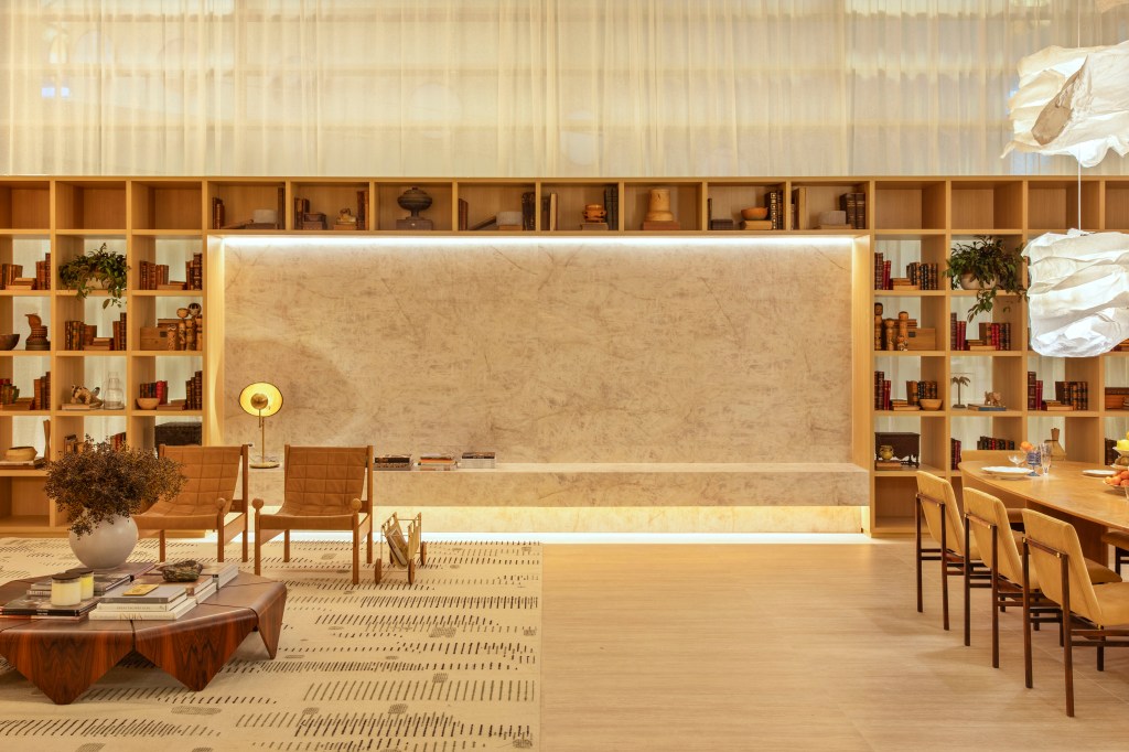 Quiet luxury e feng shui indiano marcam este loft de 120 m², Projeto de Bianca Da Hora Arquitetura para a CASACOR SP 2023. Na foto, sala com parede de pedra, estante, mesa, cadeiras e tapete.