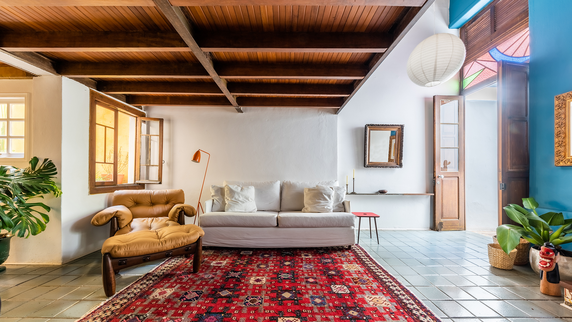 Reforma em casa 100 m² resgata a arquitetura do início do século XX. Projeto Meridional Arquitetura. Na foto, sala com sofá, teto de madeira, tapete e poltrona mole.