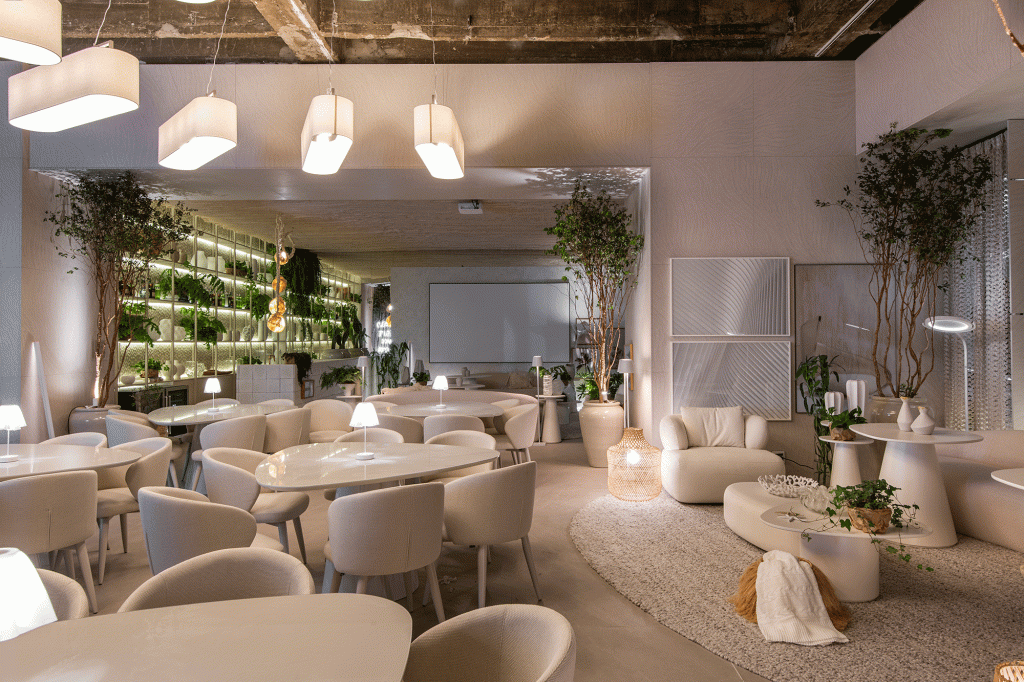 Restaurante grego em SP é inspirado na arquitetura de Mykonos. Projeto de Carla Felippi para a CASACOR São Paulo 2023. Na foto, mesas e cadeira curvas, tapete e arvores.