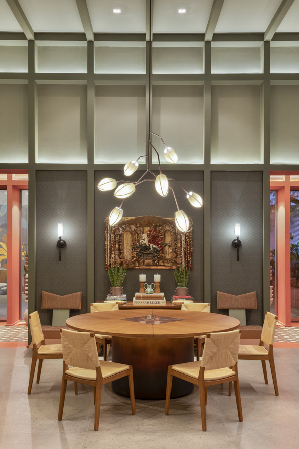 Sala de jantar com parede verde, mesa redonda de madeira, luminária.