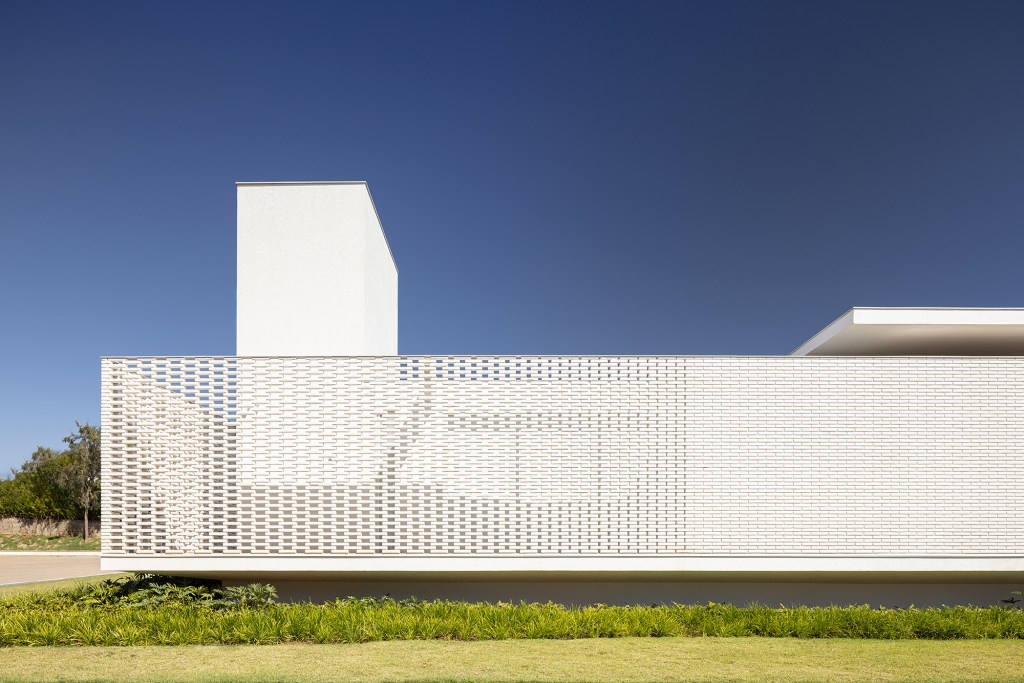 Tijolos vazados brancos compõem a fachada desta casa de 600 m² em Brasília. Projeto de Bloco Arquitetos. Na foto, fachada vazada com blocos vazados e jardim.