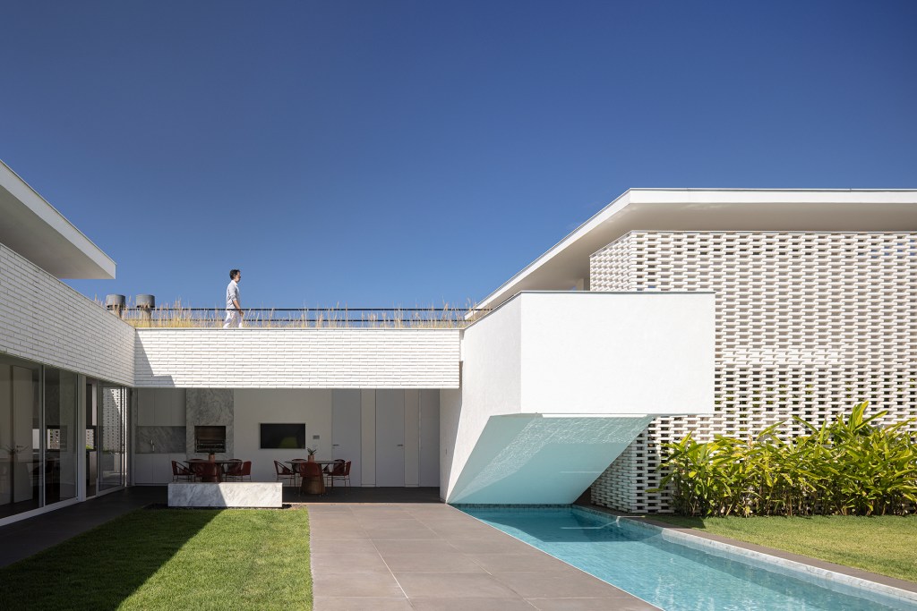 Tijolos vazados brancos compõem a fachada desta casa de 600 m² em Brasília. Projeto de Bloco Arquitetos. Na foto, fachada vazada com blocos vazados, jardim e piscina.