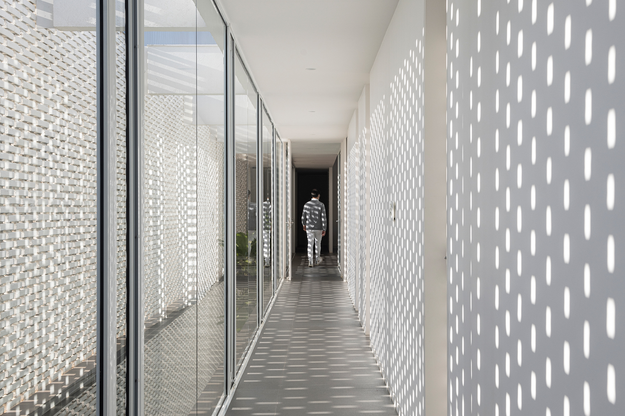 Tijolos vazados brancos compõem a fachada desta casa de 600 m² em Brasília. Projeto de Bloco Arquitetos. Na foto, corredor com efeito de luz provocado pela parede de tijolos vazados.