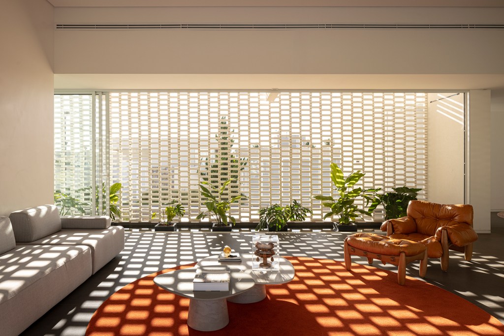 Tijolos vazados brancos compõem a fachada desta casa de 600 m² em Brasília. Projeto de Bloco Arquitetos. Na foto, sala de estar com parede de tijolos vazados e tapete laranja.