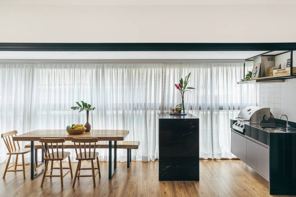 Sala de jantar; área gourmet com mesa de madeira, bancada preta com pia e churrasqueira.