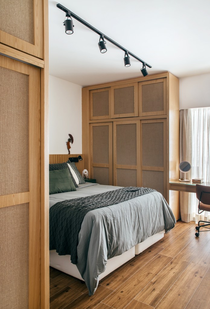 Quarto com cama de casal, cabeceira de madeira e armários com porta revestidas de juta.