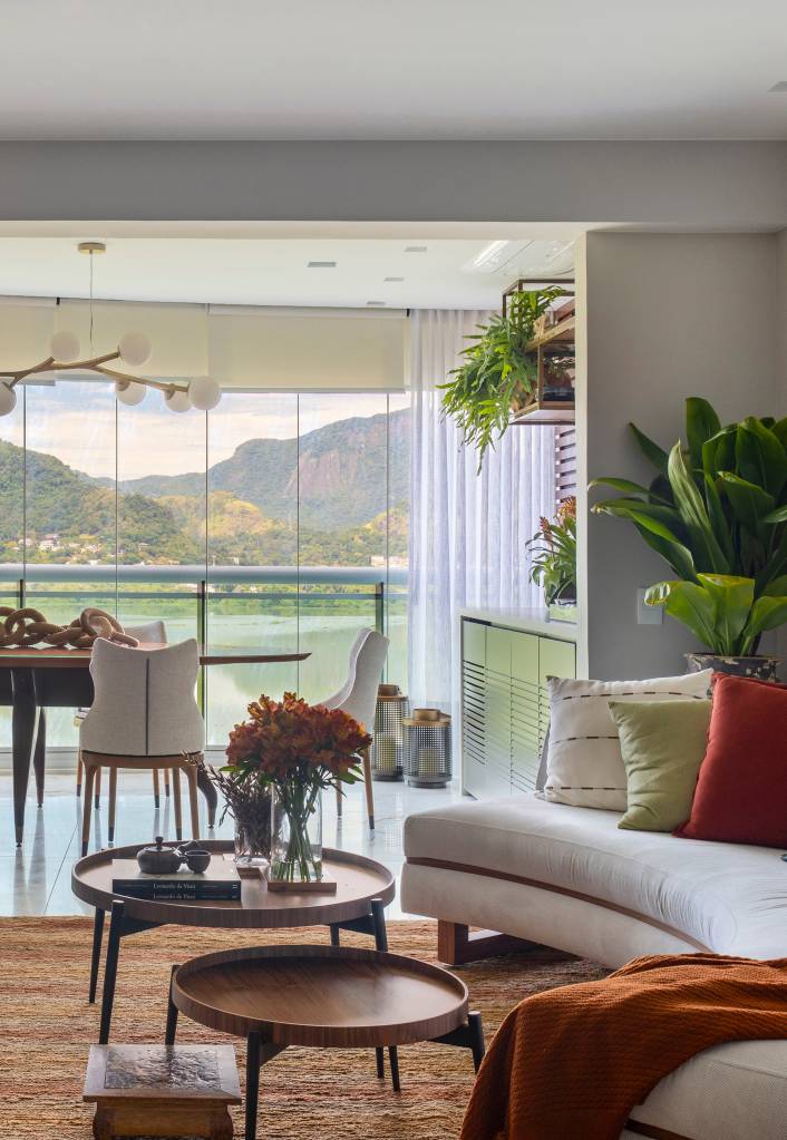 Sala de estar integrada com varanda, piso de porcelanato marmorizado, sofá curvo claro e tapete terracota;