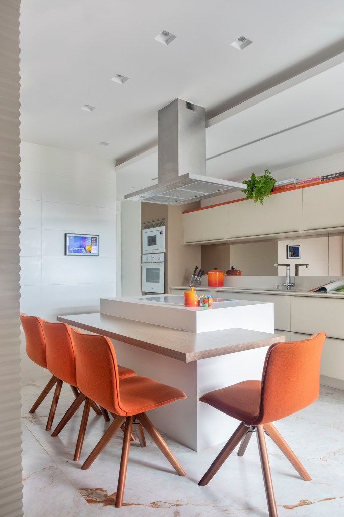 Cozinha integrada com marcenaria branca, piso marmorizado, banquetas laranja.