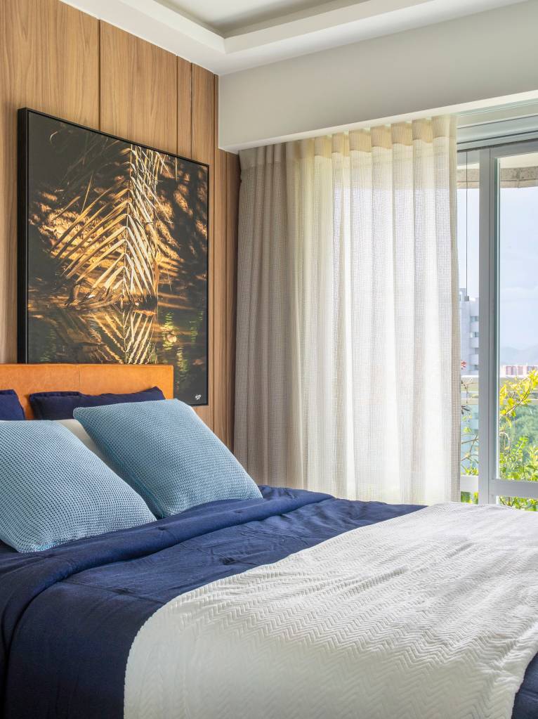 Quarto com cama de casal, cortina e parede revestida de madeira com quadro.