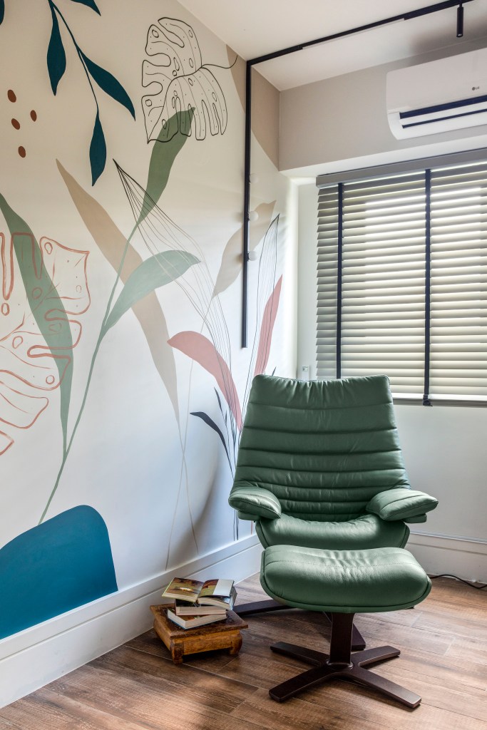 Home office com mural botânico e poltrona verde.