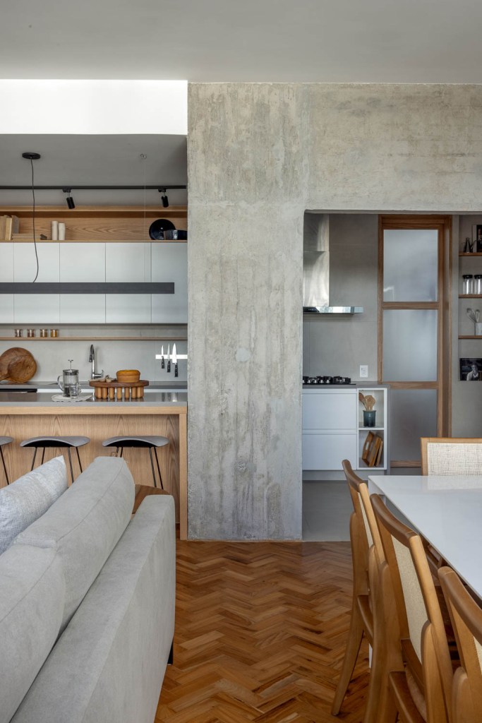 Cozinha integrada com marcenaria branca e viga de concreto.