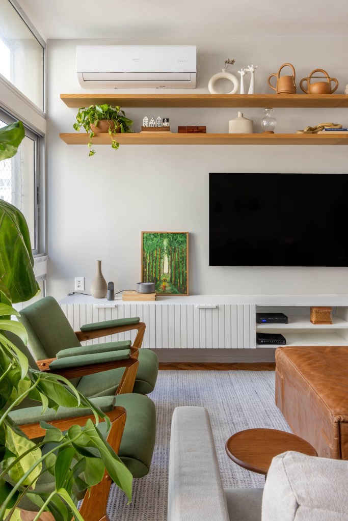 Sala de tv com parede e rack brancos, pufe como mesa de centro e poltronas verdes.