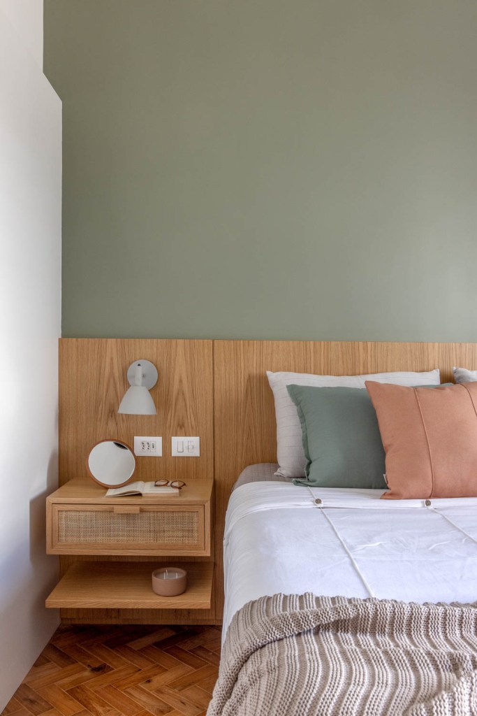 Quarto com cabeceira de madeira, mesa lateral e parede verde.