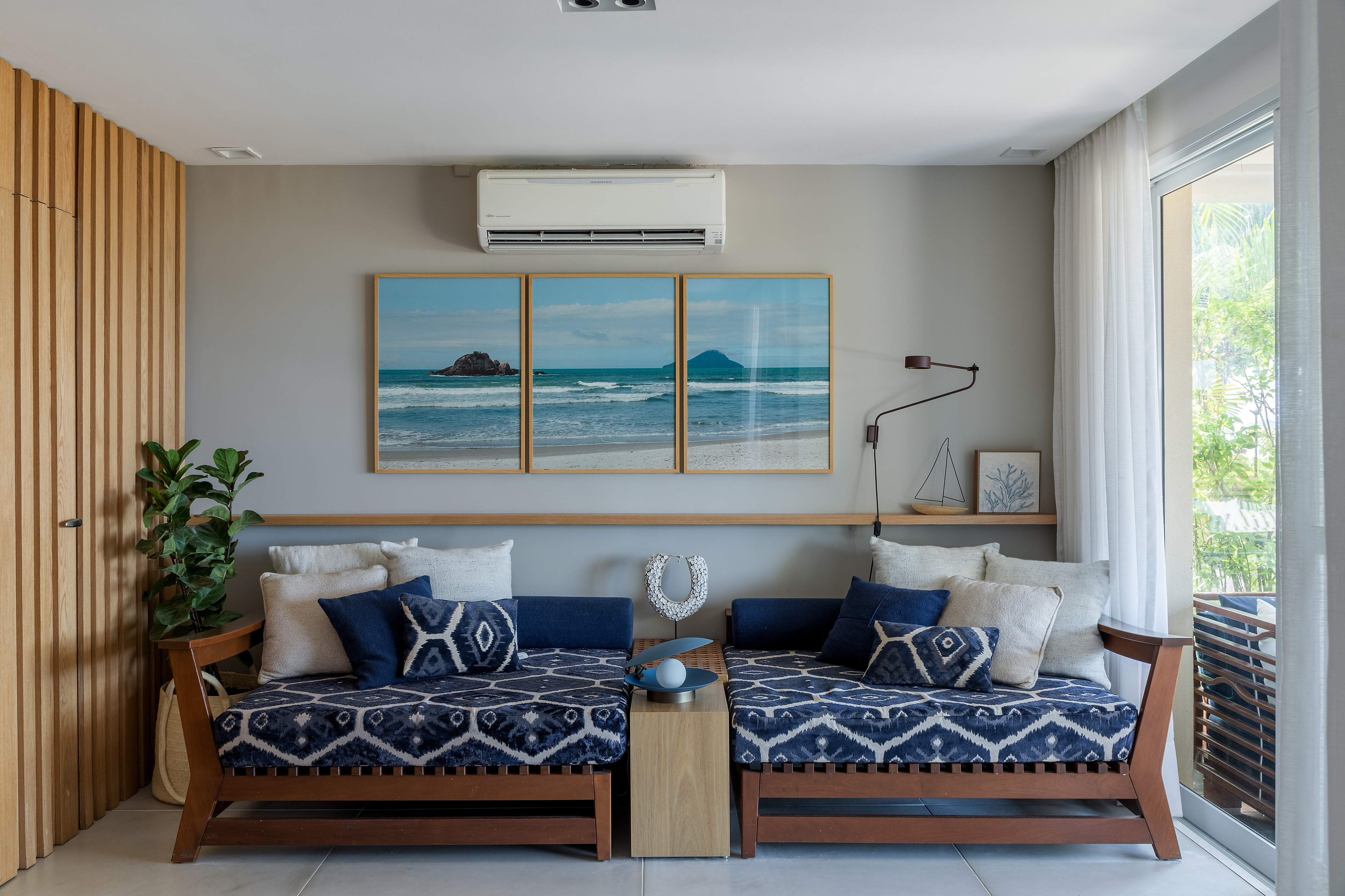 A vista da sala desta casa de praia é o mar de Juquehy. Projeto de Beatriz Quinelato. Na foto, sala com chaise azul, parede ripada e vista pra varanda.