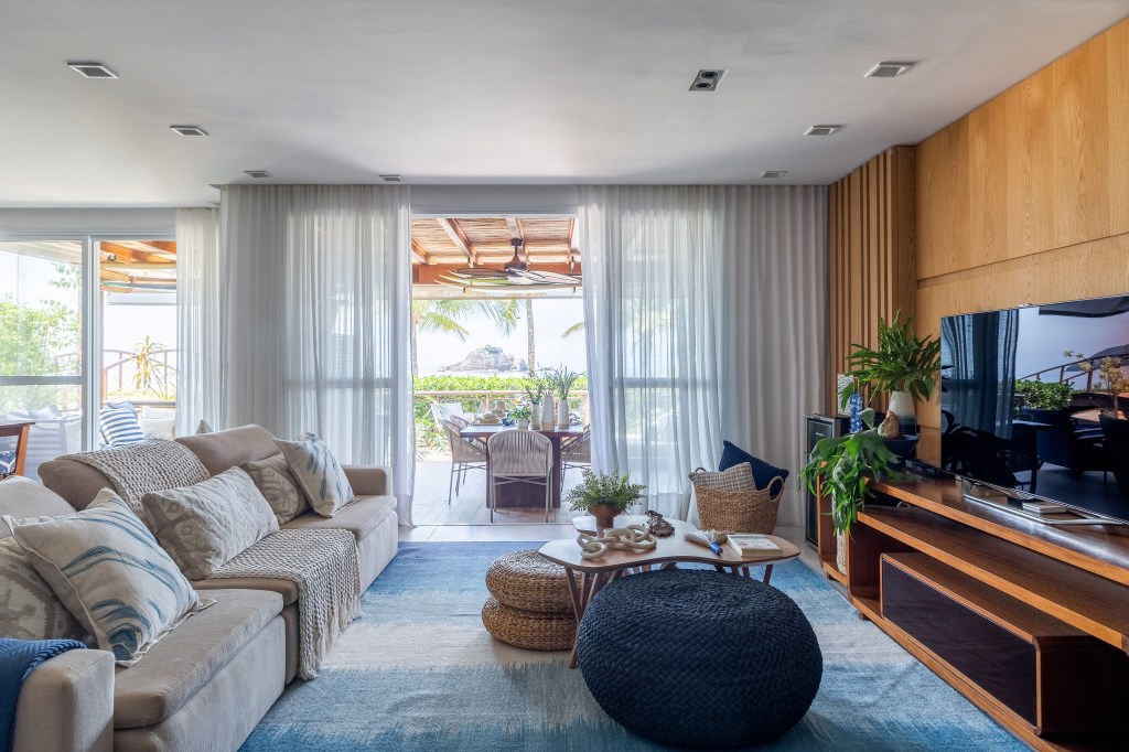 A vista da sala desta casa de praia é o mar de Juquehy. Projeto de Beatriz Quinelato. Na foto, sala com vista para omar, tapete azul, tv e varanda integrada.