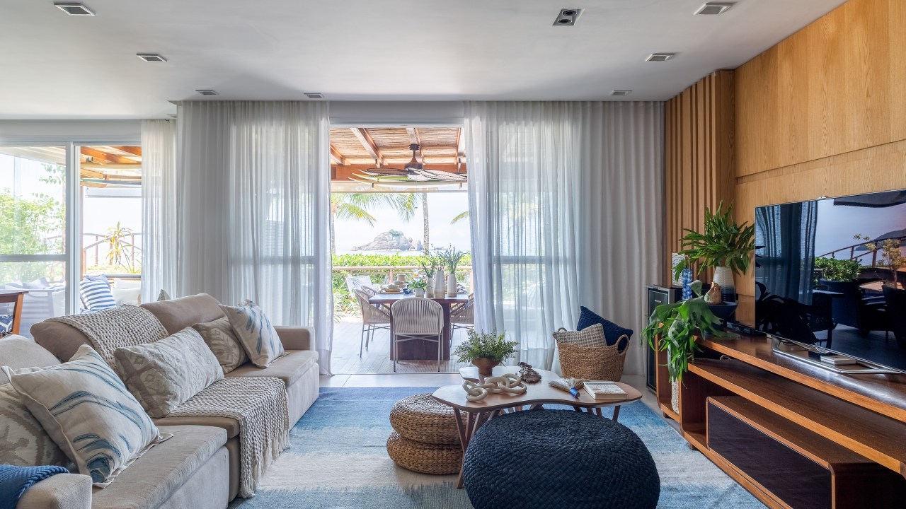 A vista da sala desta casa de praia é o mar de Juquehy. Projeto de Beatriz Quinelato. Na foto, sala com vista para omar, tapete azul, tv e varanda integrada.