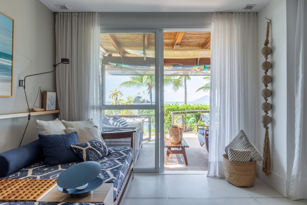 A vista da sala desta casa de praia é o mar de Juquehy. Projeto de Beatriz Quinelato. Na foto, sala com chaise, obras de arte e varanda integrada.