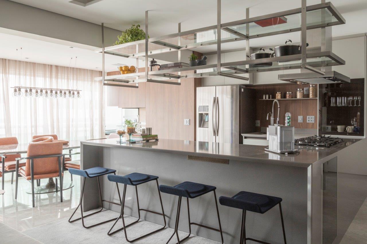 Cozinha integrada com marcenaria cinza, bancada e banquetas azuis e parede revestida de madeira.