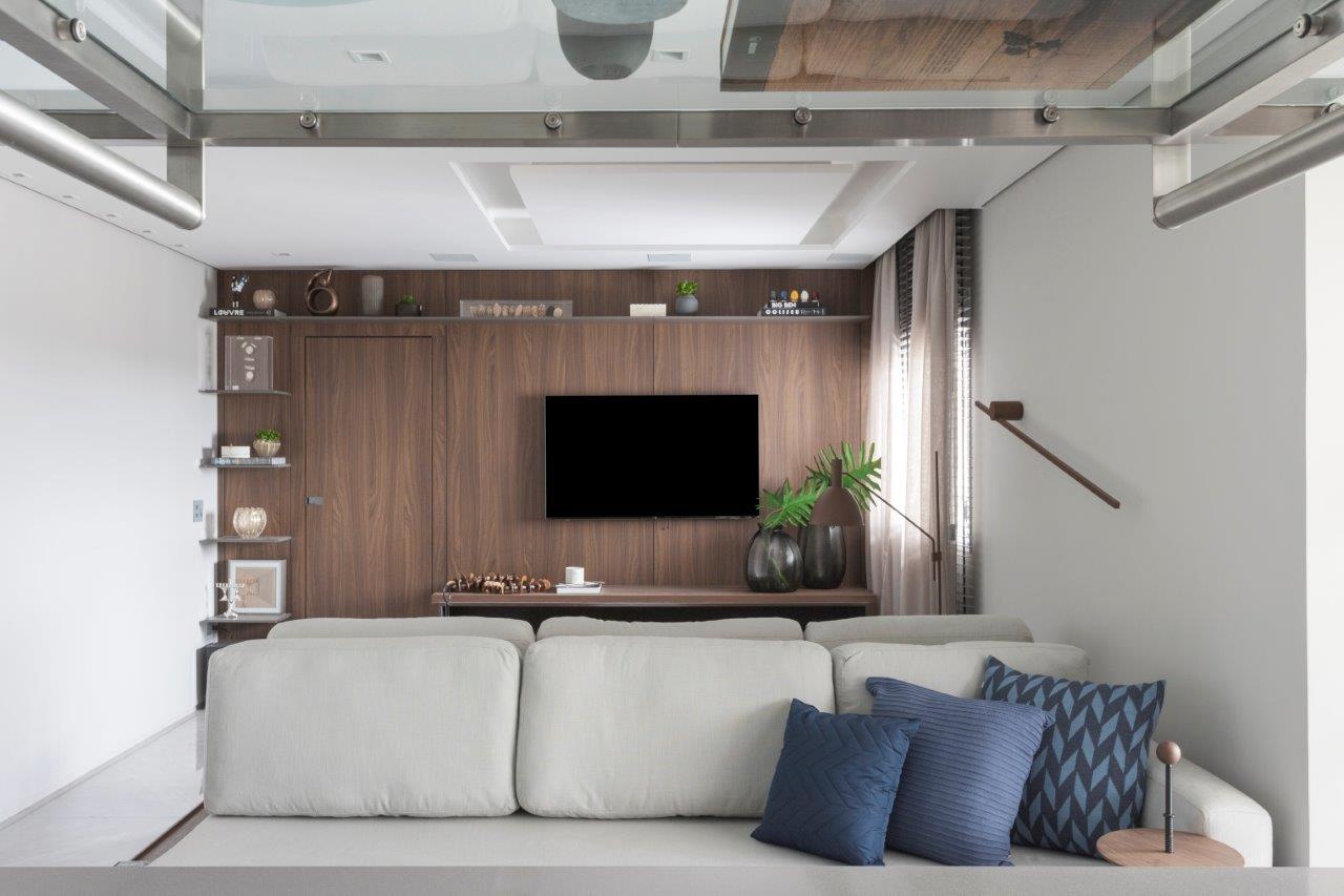 Sala de estar com parede revestida com painel de madeira e sofá cinza.