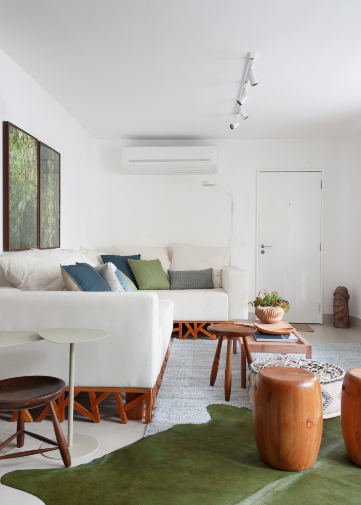 Projeto de Ricardo Melo e Rodrigo Passos. Na foto, sala de estar com sofá branco, trilho de spot e tapete verde.