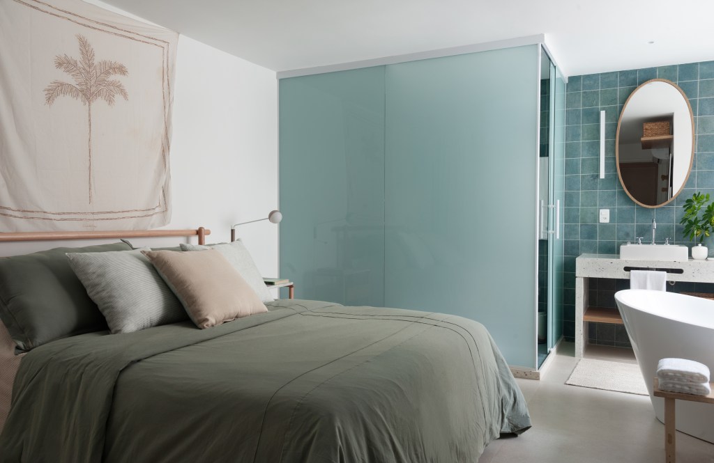 Projeto de Ricardo Melo e Rodrigo Passos. Na foto, quarto com cama de casal, mesa lateral e tecido estampado com palmeira sobre a cama.