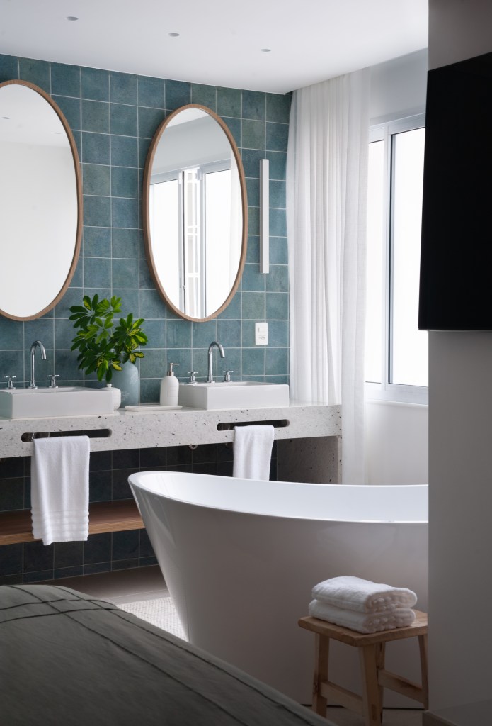 Projeto de Ricardo Melo e Rodrigo Passos. Na foto, banheiro revestido com pedra hijau verde, banheira solta, espelho oval e cuba dupla.
