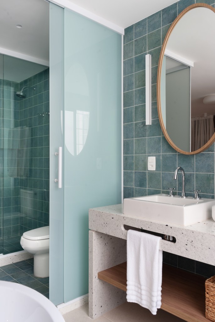 Projeto de Ricardo Melo e Rodrigo Passos. Na foto, banheiro revestido com pedra hijau verde, banheira solta, espelho oval e cuba dupla.
