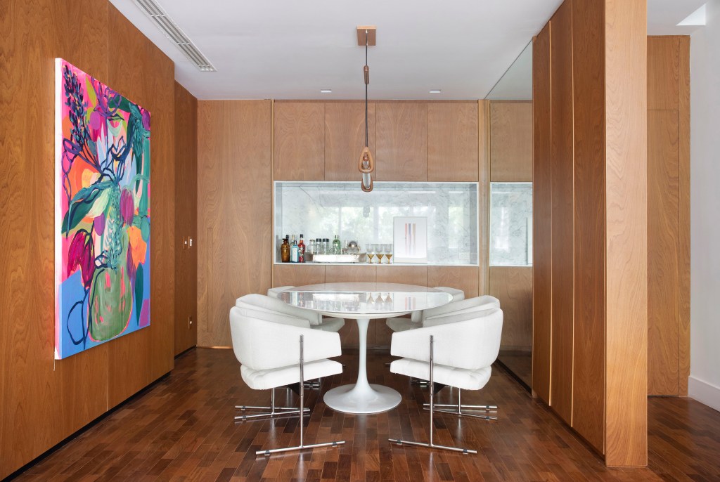 Projeto de Bianca Da Hora. Na foto, sala de jantar com mesa oval branca, cadeiras brancas estofadas, lustre e paredes revestidas de madeira.