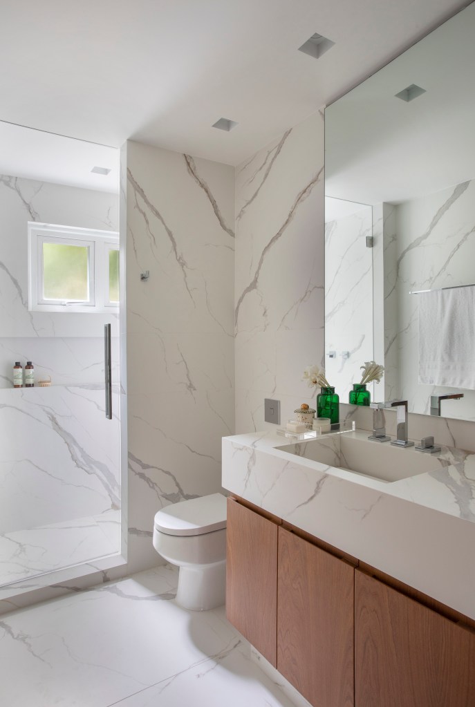 Projeto de Bianca Da Hora. Na foto, banheiro branco com cuba esculpida e revestimento marmorizado.