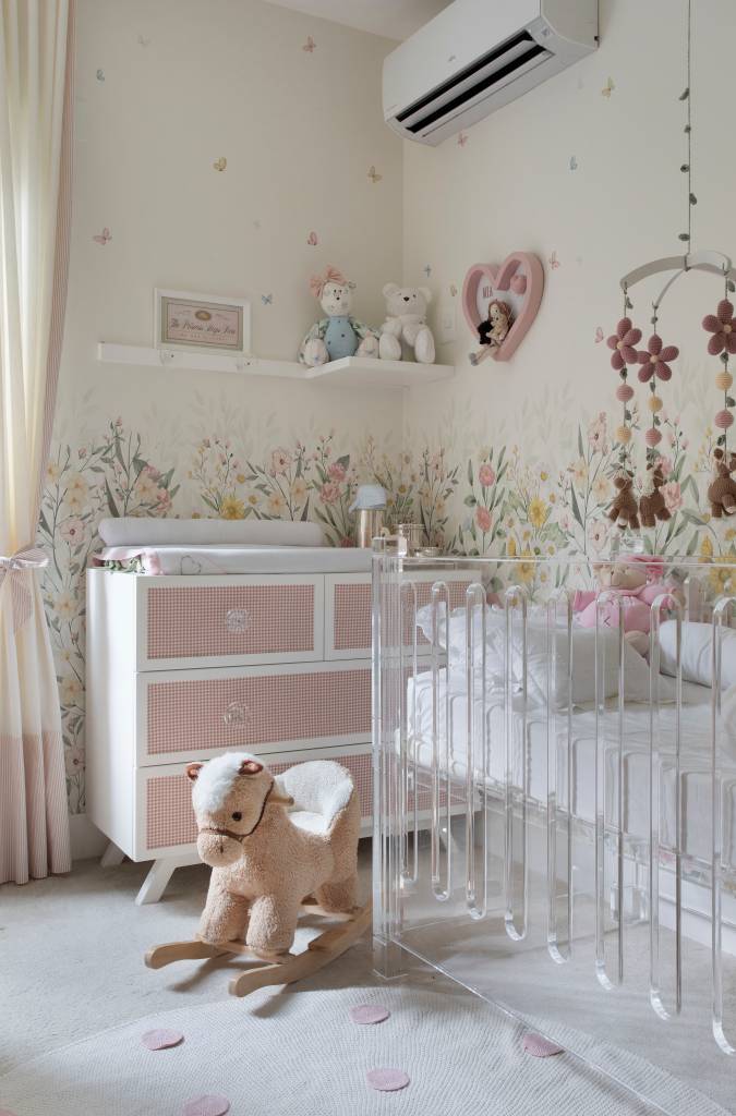 Projeto de Bianca Da Hora. Na foto, quarto de bebê com papel de parede floral, poltrona branca, sofá cama e berço de acrílico branco.