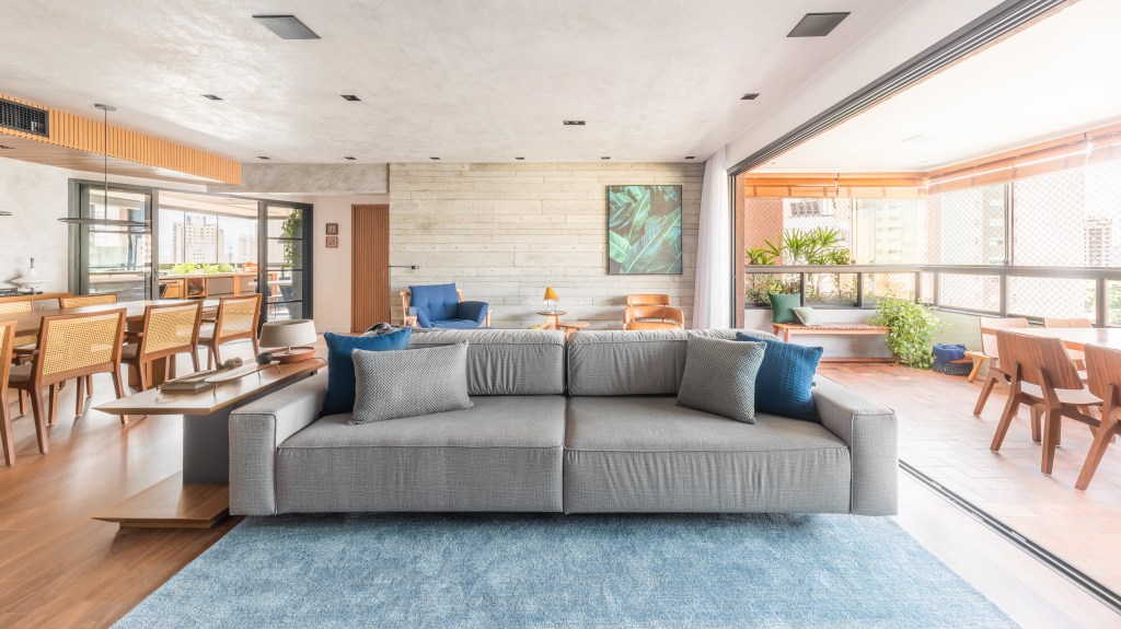 Projeto de Pietro Terlizzi. Na foto, sala de estar integrada com tapete azul, sofá ilha cinza.