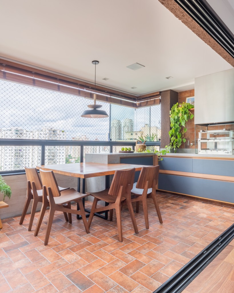 Projeto de Pietro Terlizzi. Na foto, varanda integrada gourmet com mesa de madeira e churrasqueira.