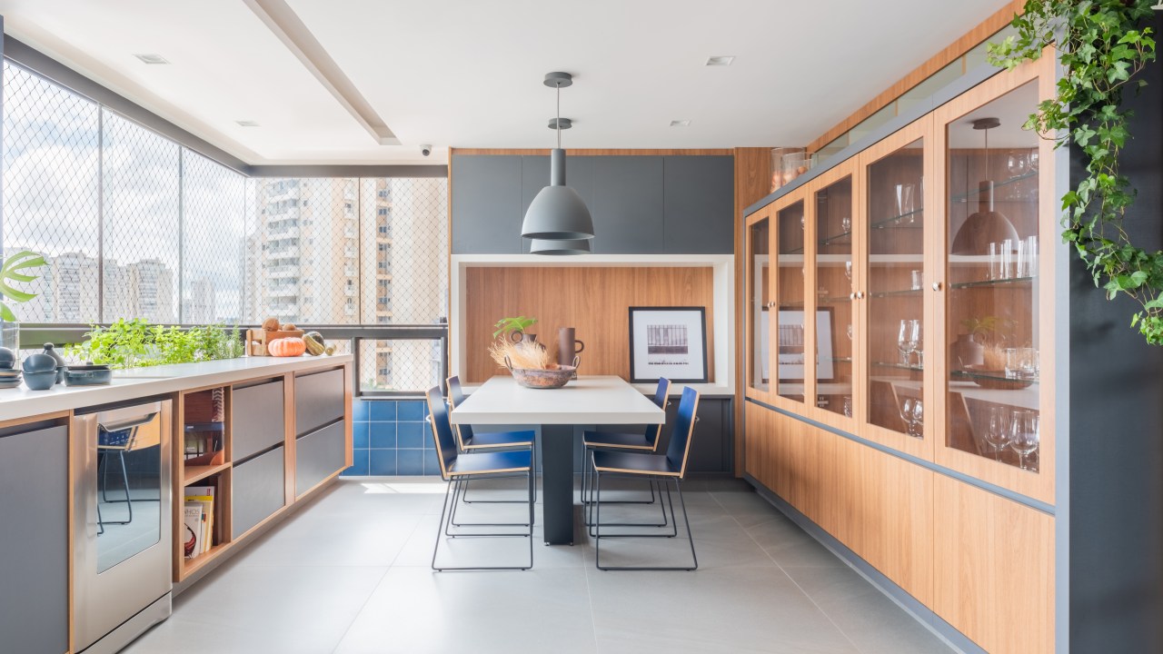 Projeto de Pietro Terlizzi. Na foto, varanda integrada com cozinha com cristaleira, mesa para refeições, piso de porcelanato e parede de azulejos azuis.