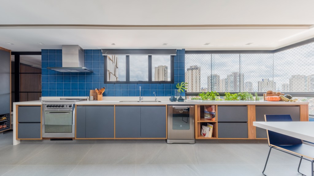Projeto de Pietro Terlizzi. Na foto, cozinha integrada com piso de porcelanato, marcenaria cinza e parede de azulejos azuis.