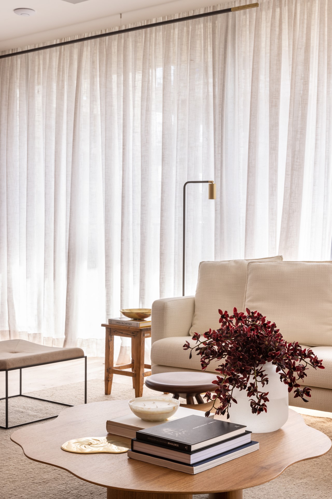 Projeto de Denise Polverini e Fernanda Villefort. Na foto, sala de estar em tons beges com tapete, mesa de centro de madeira e sofá branco.