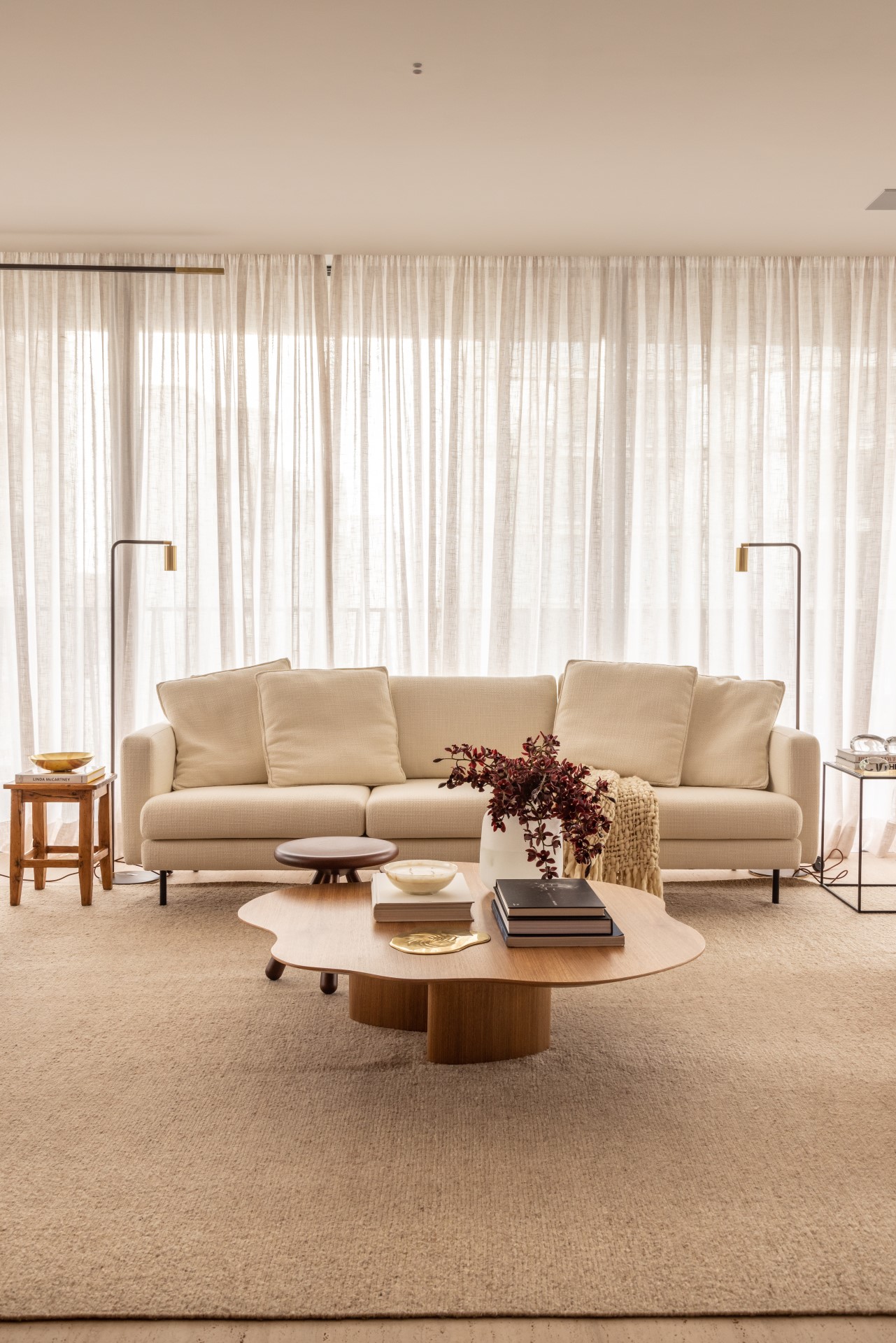 Projeto de Denise Polverini e Fernanda Villefort. Na foto, sala de estar em tons beges com tapete, mesa de centro de madeira e sofá branco.