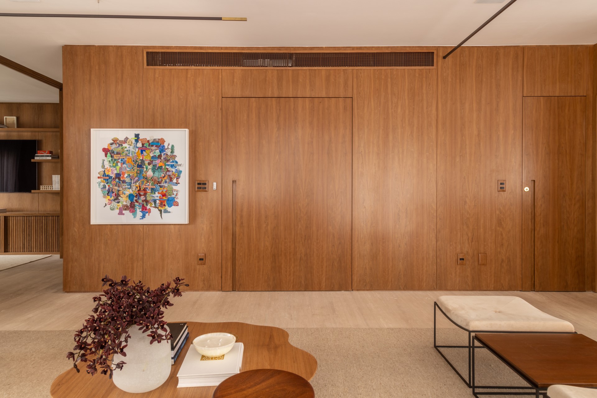 Projeto de Denise Polverini e Fernanda Villefort. Na foto, sala de estar com parede revestida de madeira e porta pivotante.