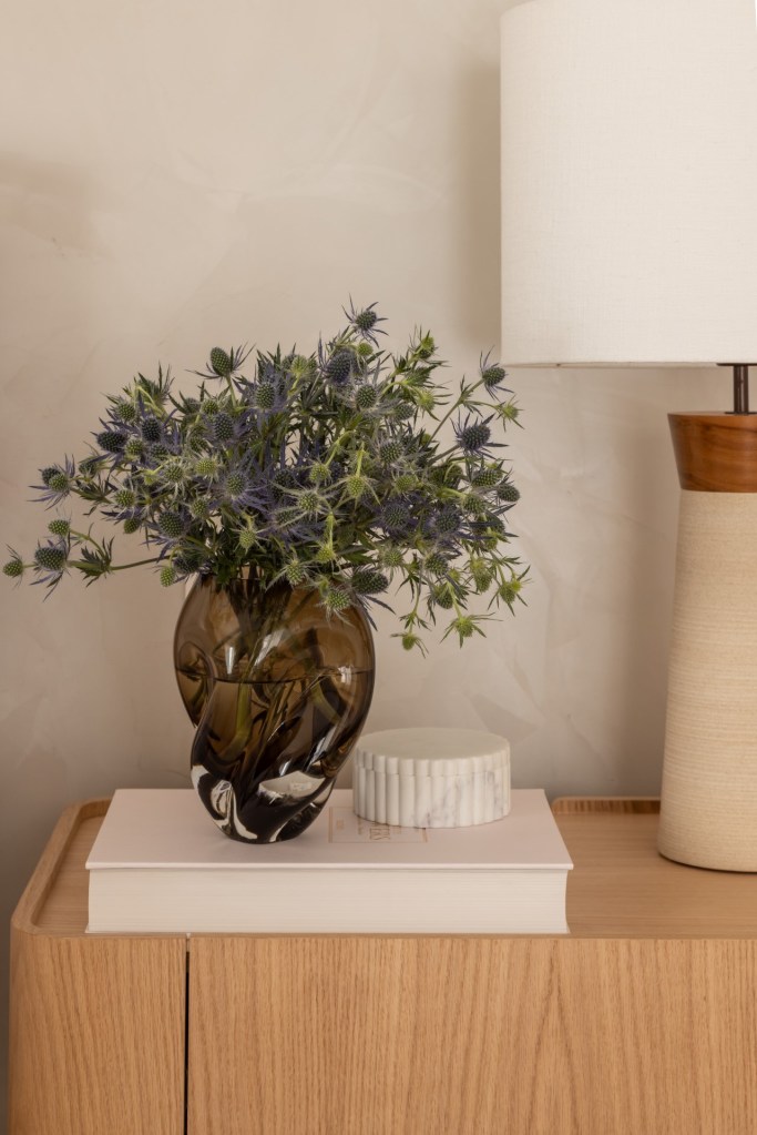 Projeto de Denise Polverini e Fernanda Villefort. Na foto, mesa lateral com abajur, vaso de planta e livro.