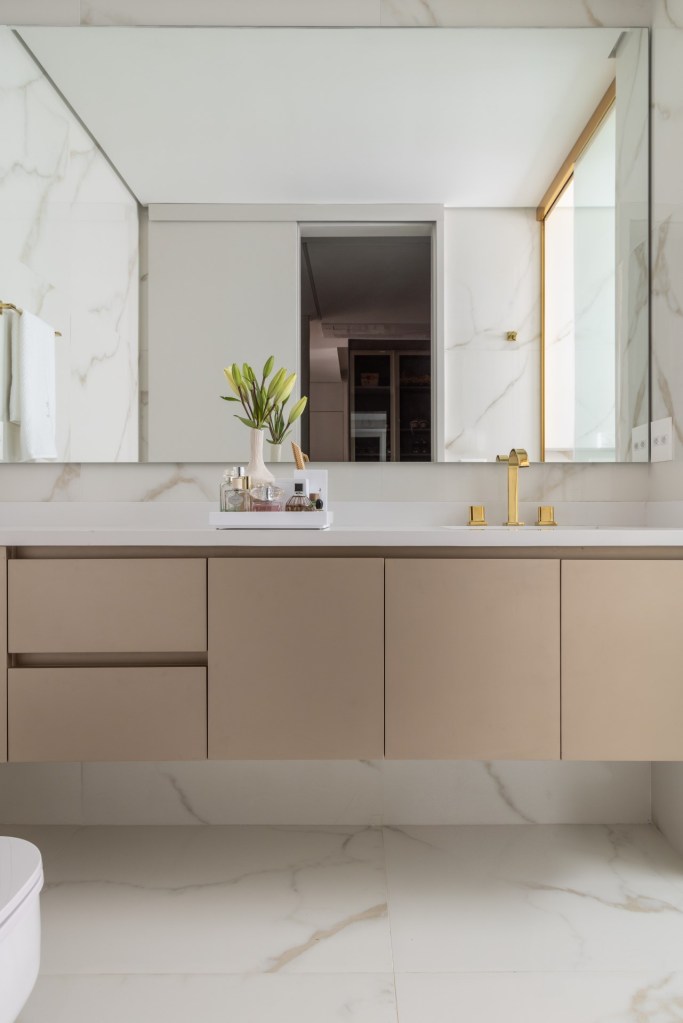 Projeto de Denise Polverini e Fernanda Villefort. Na foto, banheiro com espelho, metais dourados e armário bege.